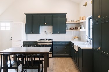 Minimalist kitchen with gray cabinets, farmhouse sink, white tile backsplash, and wood shelves